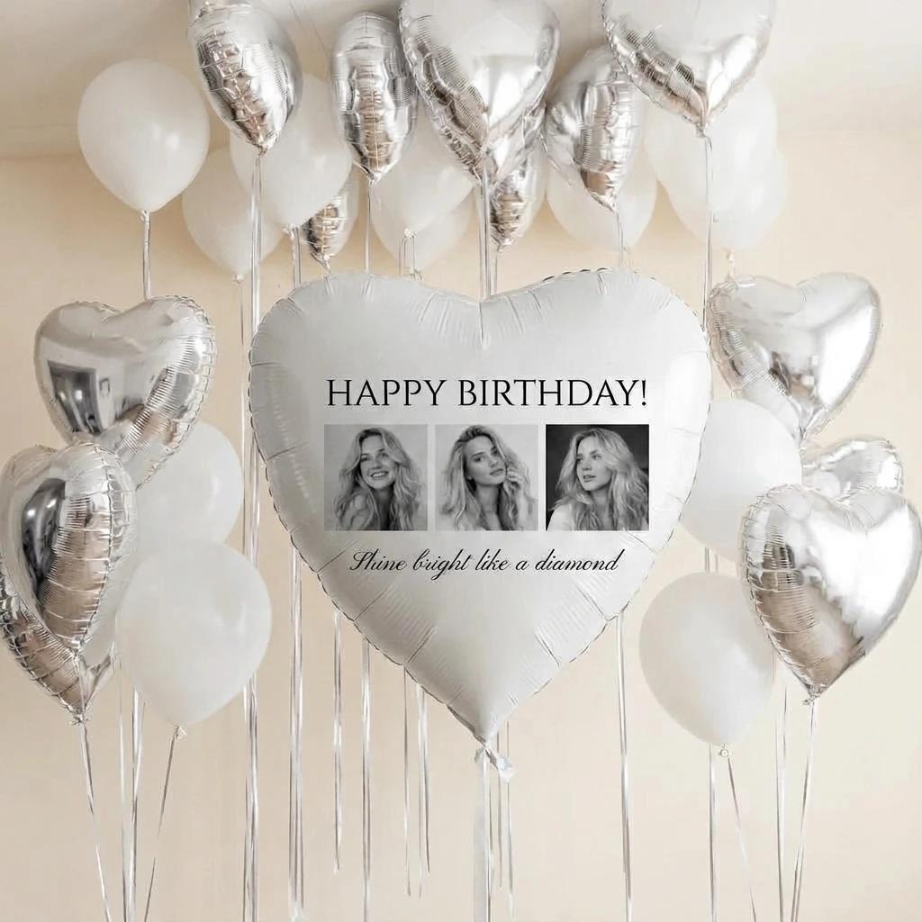 A set of heart-shaped and round balloons, including a large central white heart balloon printed with 'HAPPY BIRTHDAY!' and two black-and-white portrait photos, surrounded by smaller white and reflective silver balloons against a plain light beige background.