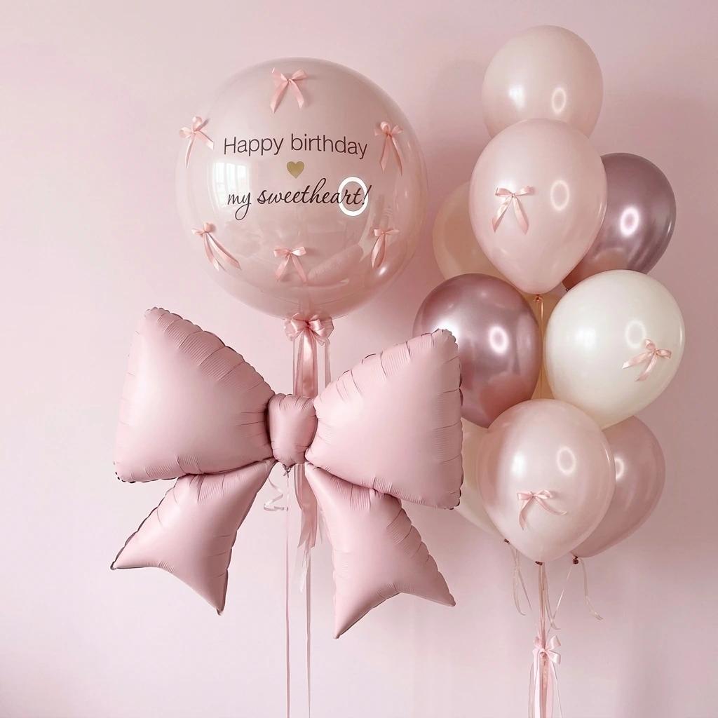 Pink birthday balloon bouquet with a large pink foil bow, a clear round balloon reading 'Happy birthday my sweetheart!' with small pink bow details, and a cluster of blush, cream, and rose-gold balloons against a soft pink background.