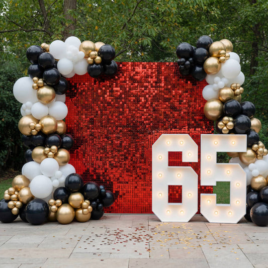 A glamorous black-white-gold balloon garland with a red shimmer wall and marquee numbers - a bold, elegant backdrop for milestone celebrations.