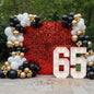 A glamorous black-white-gold balloon garland with a red shimmer wall and marquee numbers - a bold, elegant backdrop for milestone celebrations.